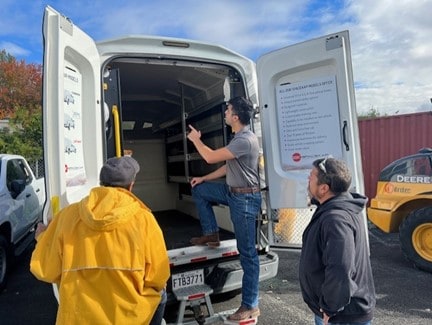 Trois hommes regardant l'intérieur d'un camion utilitaire blanc avec les portes arrière ouvertes