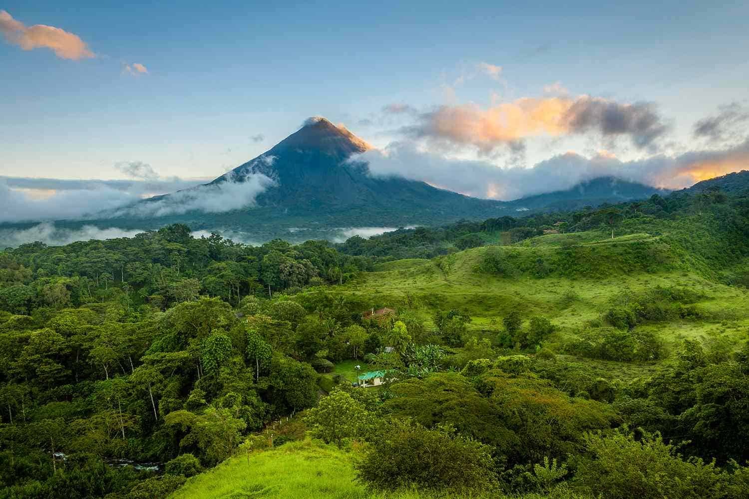 Volcan entouré de collines verdoyantes et forêt dense sous un ciel bleu partiellement nuageux
