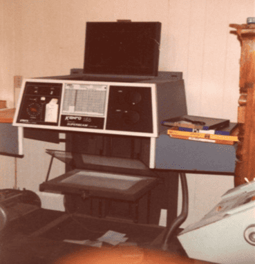 Ancienne machine de reprographie avec boutons et écran, sur un support en bois dans une pièce aux murs en bois clair
