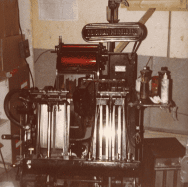 Ancienne machine d'impression mécanique avec plusieurs rouleaux et leviers dans une pièce.