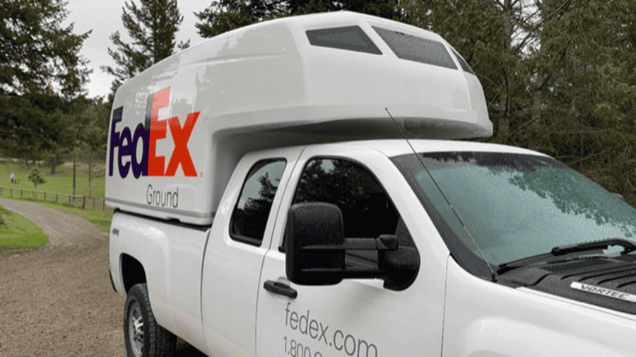 Camionnette blanche avec compartiment supérieur FedEx Ground garée sur un chemin de gravier avec des arbres en arrière-plan