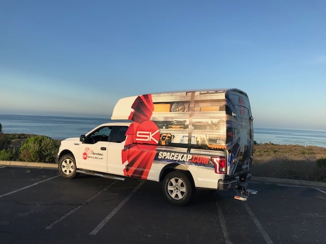 Camionnette blanche avec lettrage publicitaire rouge et noir stationnée près de la mer au coucher du soleil