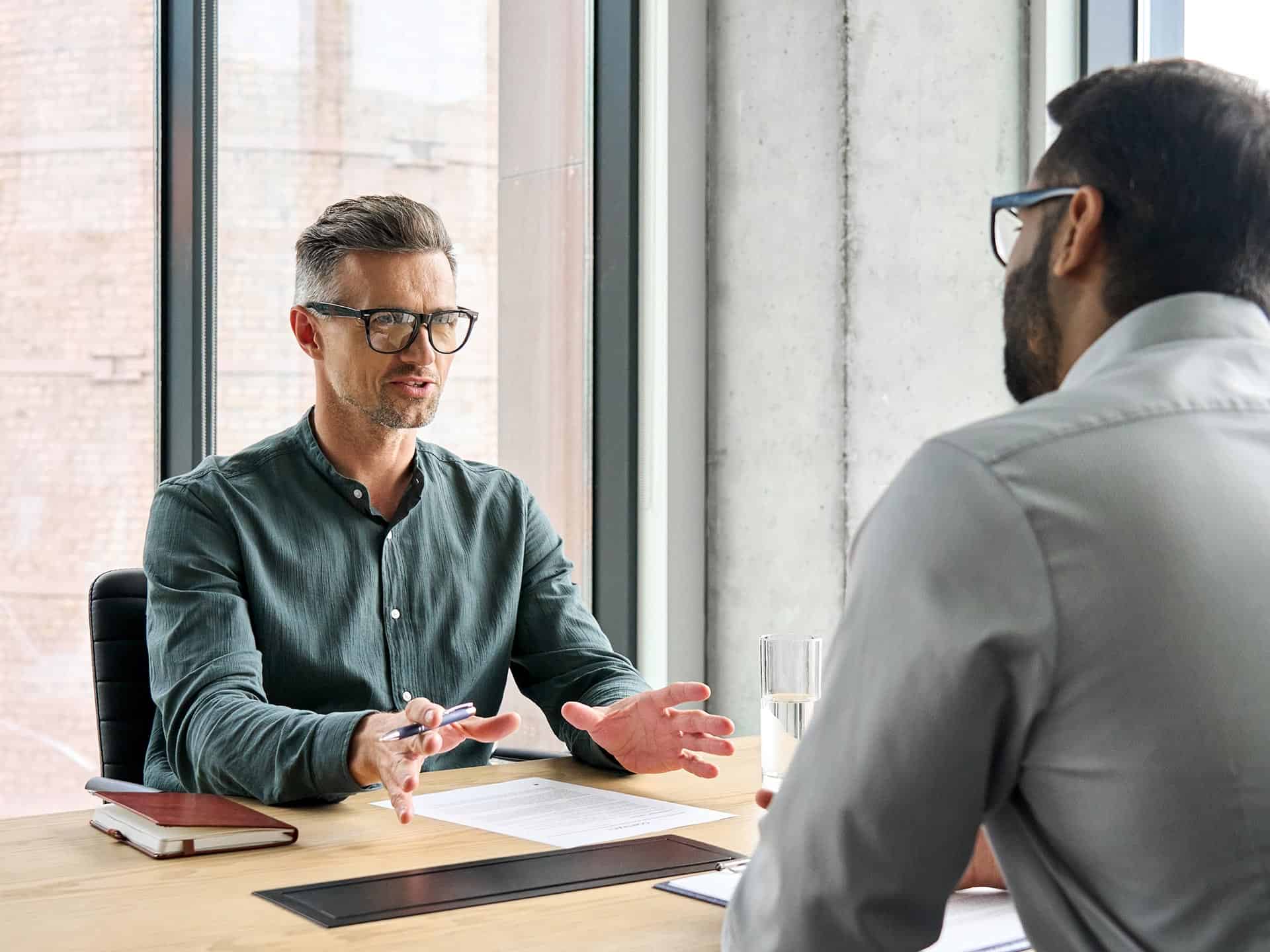 Deux hommes en discussion professionnelle dans un bureau lumineux près d'une fenêtre